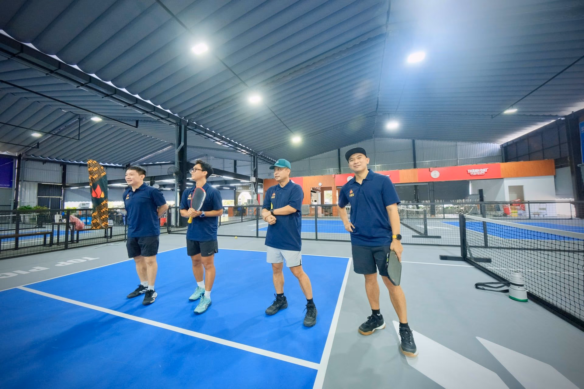 Four Training Club coaches in navy polos standing together on an indoor court.