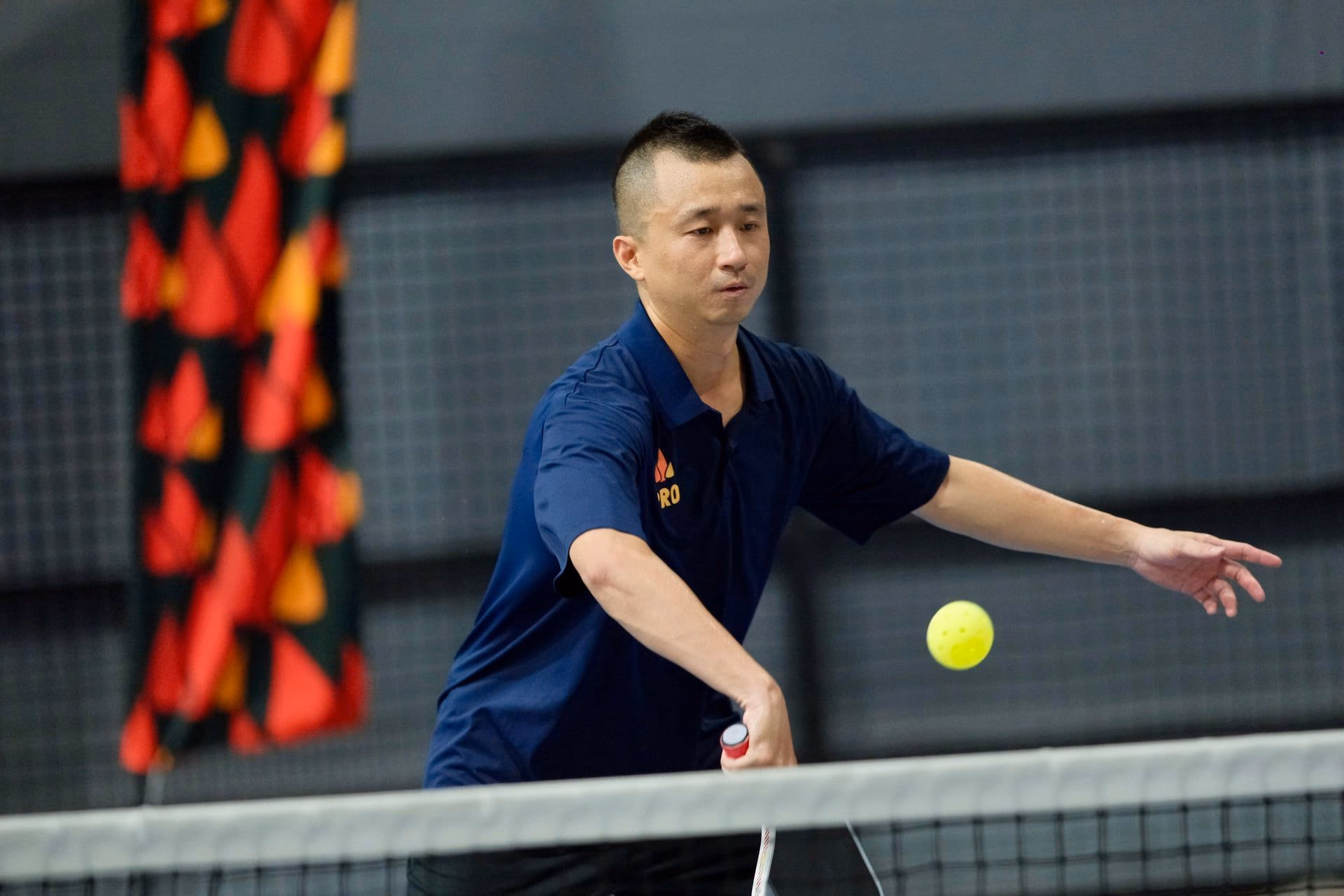A coach in a Training Club polo reaching wide for a forehand at the net.